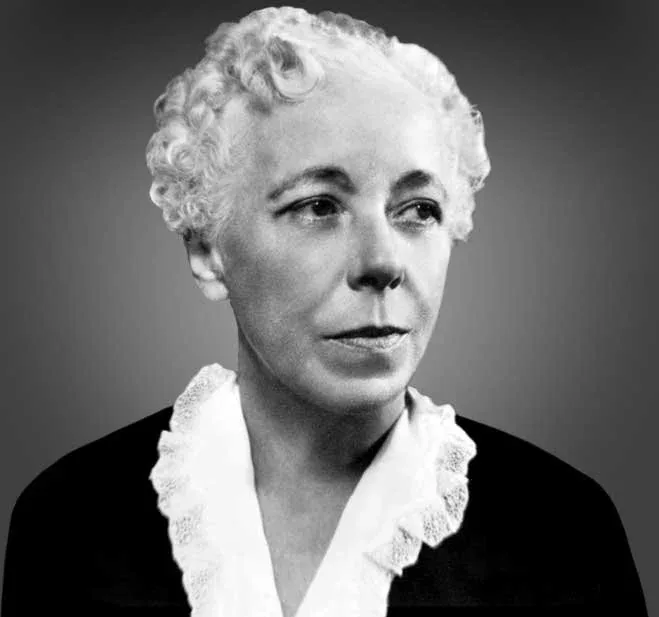 Black-and-white portrait photograph of Karen Horney, a middle-aged woman with short, curly white hair. She wears a dark blouse with a white ruffled collar and looks slightly off-camera with a calm, composed expression.