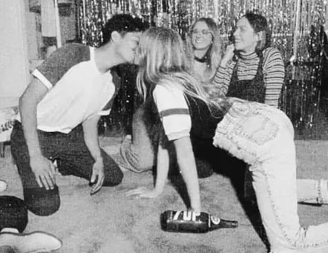 A group of teenagers playing spin the bottle at a party in the 1960s.