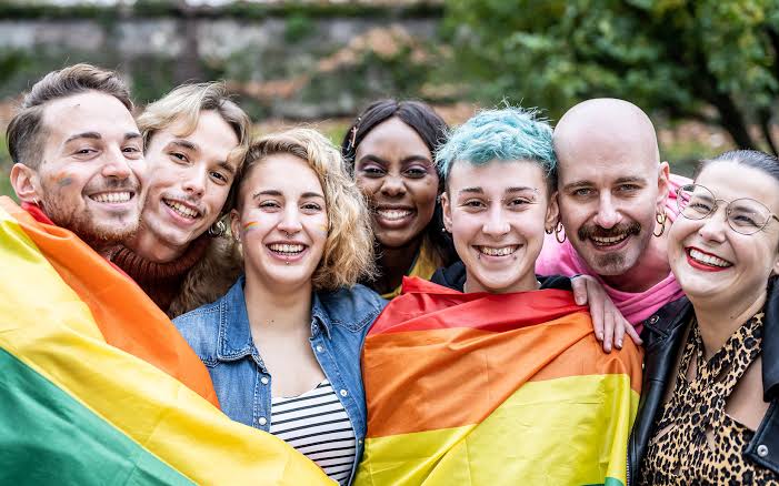 A diverse group of LGBTQ+ people of different ages, races, and gender presentations.