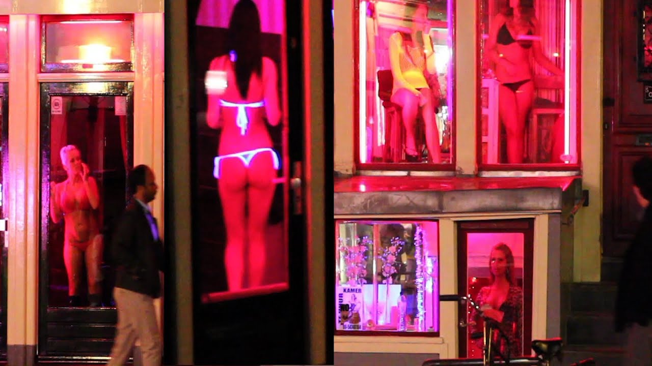 Amsterdam red-light district at night with women in lingerie in red-lit windows and a man walking by.