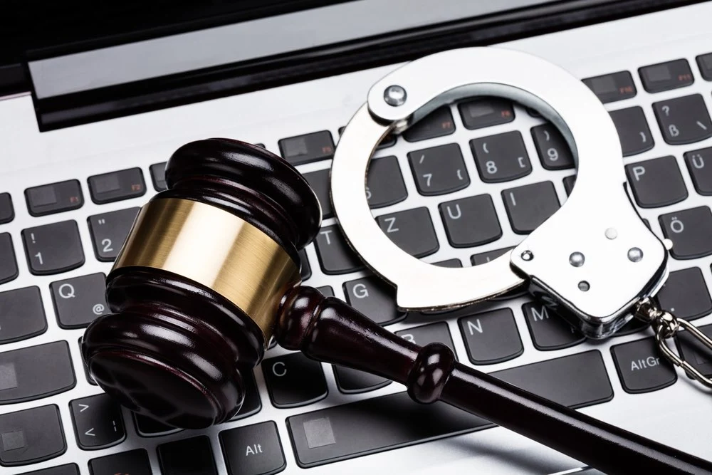 A wooden gavel and metal handcuffs resting on a laptop keyboard.