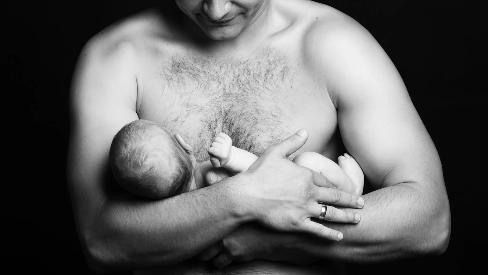 A father holding a baby skin-to-skin against his chest.