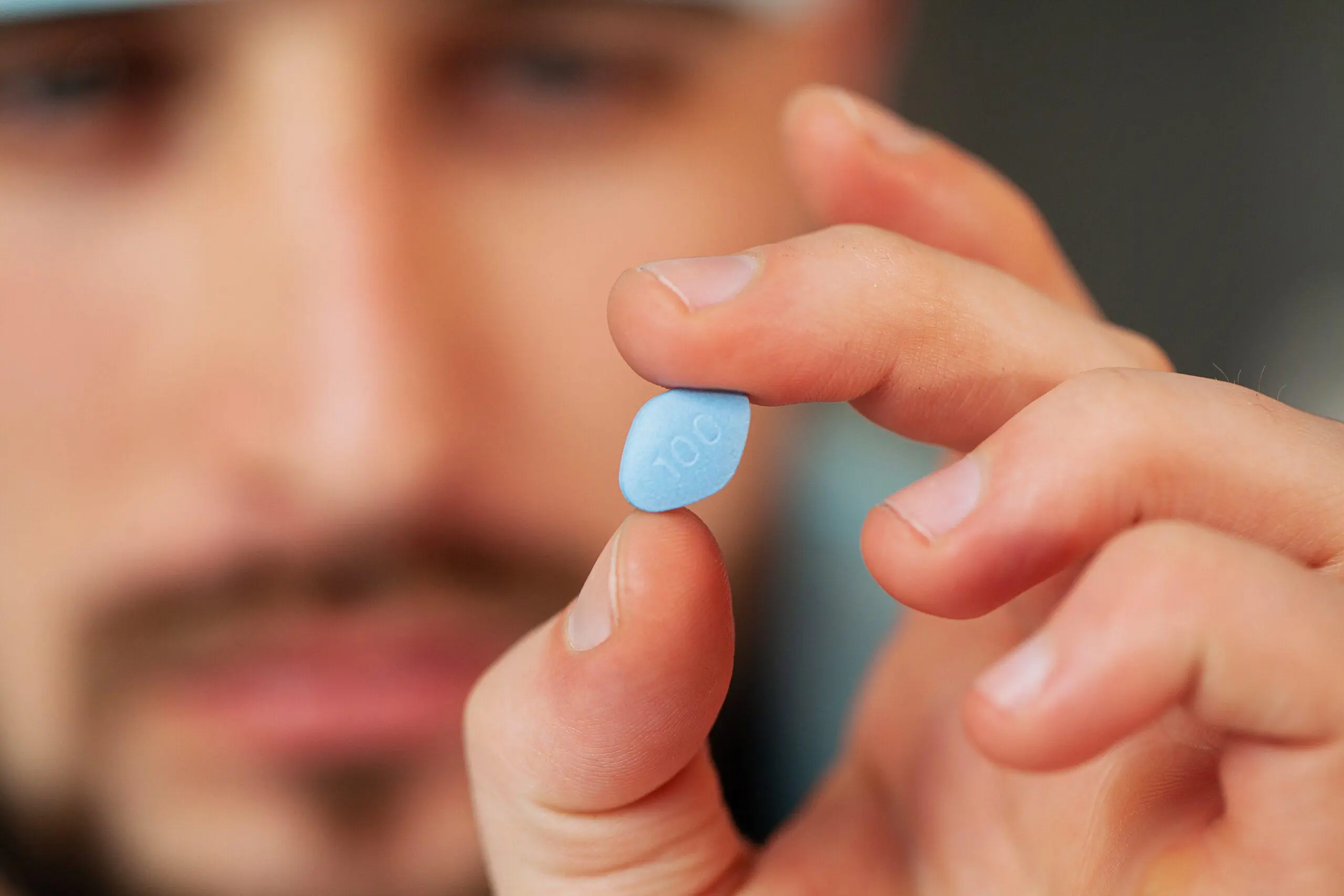 A hand holding a blue Viagra tablet.